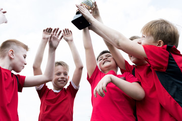 Portrait of junior football team holding trophy together and cheering happily after winning match