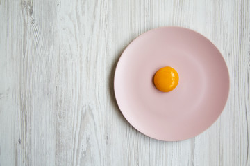 Egg yolk on a pink plate on a white wooden background, top view. Copy space and text area.