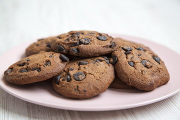 Chocolate cookies on a pink plate on a white wooden table, side view. Closeup.
