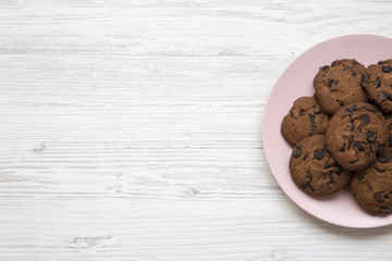 Top view chocolate chip cookies on a pink plate on a white wooden background. Copy space.