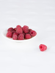 Fresh ripe raspberries on a white plate on a white background. Close-up,  minimal concept of fashionable food, copyspase