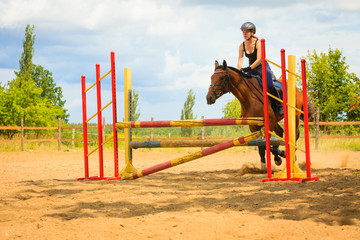 Jockey young girl doing horse jumping through hurdle