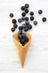 Flat-lay of waffle sweet ice cream cone with blueberries on a white wooden background.