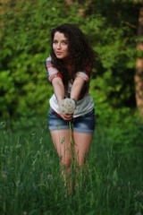 Naklejka na ściany i meble Young woman with dark curly hair. Young woman with dandelions in hands.