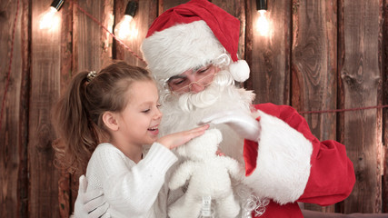 Obraz premium Little girl with teddy bear checking Santa's beard
