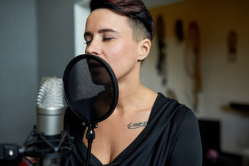 Beautiful sensual woman singing in music recording studio standing near microphone with eyes...