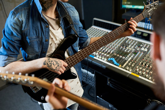 Crop shot of modern performers playing guitars in sound studio while collaborating new song. 