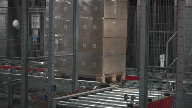 Moving conveyor belt with cardboard boxes along corridor in workplace. Clip. Boxes move along conveyor belt. Cardboard boxes picked up by a robot arm in a factory