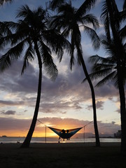 couple relaxing on a hammock between two palm trees enjoying sunset in Hawaii
