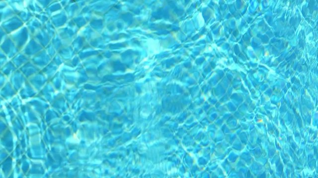 Blue water in swimming pool. Waves and patches of sunlight appears on the bottom of the pool. Glares blinks and reflections on clear water. Vertical format video.