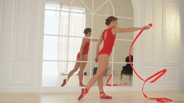 Young beautiful ballerina in red clothes, red body, red pointe shoes and with red ribbon, ballet dancer practicing with ribbon