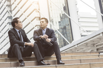 two businessmen sitting on stair discussing and talking in front of building