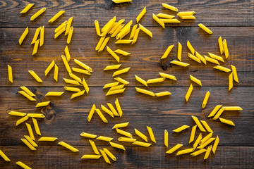 Pasta background. Raw penne on dark wooden background top view