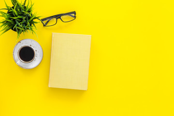 Book with empty cover near glasses, coffe, plant on yellow desk top view space for text. Spend time reading. Self-development concept.