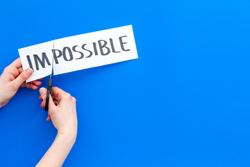 All is possible concept. Hands cutting the part im of written word impossible by sciccors. Blue background top view copy space