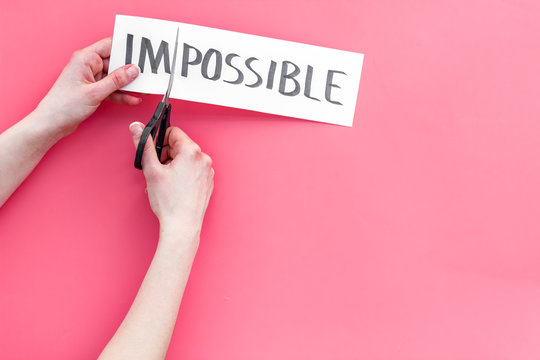 All is possible concept. Hands cutting the part im of written word impossible by sciccors. Pink background top view copy space