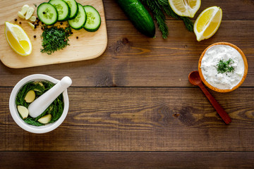 Greek yogurt as salad dressing. Bowl with yogurt, greenery, cucumber, oranges on cutting board on dark wooden kitchen desk top view space for text
