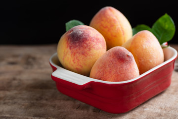 Ripe peaches in a red bowl on wooden, tropical fruit