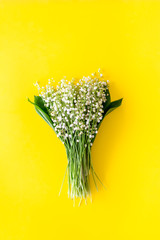 Small and fragrant spring flowers. Bouqet of lily of the valley flowers on yellow background top view copy space