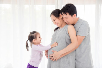 Little asian girl touching her pregnant mother belly and smiles