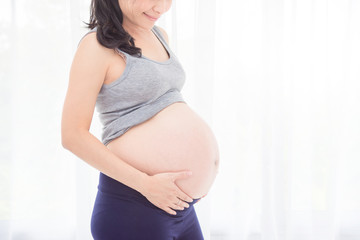 Cropped image of asian pregnant woman,holding her belly in front of bright window.