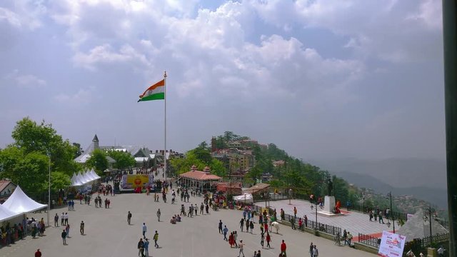 People enjoying on the ridge in shimla with the canopies and indian flag in the distance. Shot during a dusk with purple cloudy skies. The cloudy sky and the mountains in the distance showcase the
