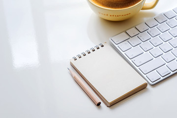 Blank note, pencil, white keyboard and cup of coffee on white table