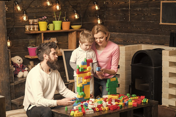 adoption of a child. Mom, dad and kid sitting around table with colorful construction bricks. Family building a house out of plastic blocks. Mother and son choosing pieces for constructing toy tower