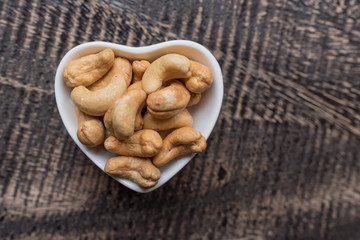 Raw cashew nuts in bowl on textured wooden background, table top view