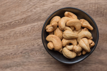 Raw cashew nuts in bowl on textured wooden background, table top view
