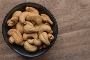 Raw cashew nuts in bowl on textured wooden background, table top view
