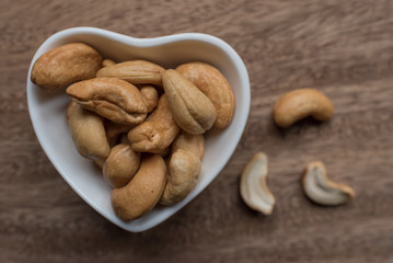 Raw cashew nuts in bowl on textured wooden background, table top view