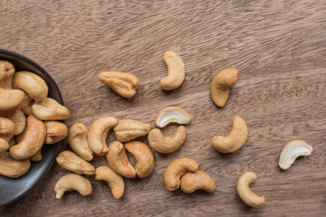 Raw cashew nuts in bowl on textured wooden background, table top view