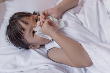 cold sick child laying on bed and blowing her nose in tissue