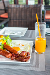 American Breakfast is foods with health benefits on table./ Bread basket, orange juice, fried egg, sausage, ham, salad, fried bacon are foods with health benefits in morning.