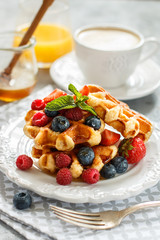Fresh homemade waffles with raspberries, strawberries, blueberries and honey. Delicious Breakfast with berries, cappuccino and orange juice