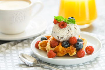 Homemade waffles with ice cream and fresh berries-raspberries, blueberries. Delicious dessert, cappuccino and orange juice on the table