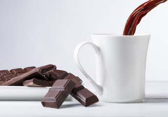 White mug of hot drink and bitter chocolate pieces.