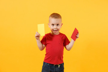 Little cute kid baby boy in red t-shirt holding in hand yellow and red soccer referee cards for...