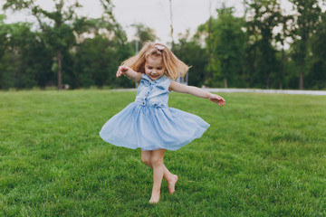 Pretty little cute child baby girl in denim dress circling around and have fun on green grass lawn...
