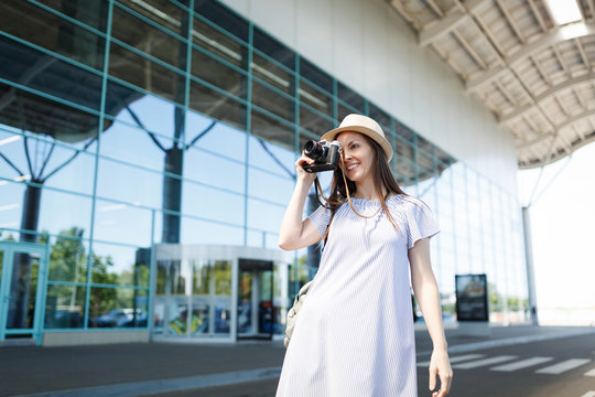 Young pretty traveler tourist woman in hat take pictures on retro vintage photo camera at international airport. Female passenger traveling abroad to travel on weekends getaway. Air flight concept.