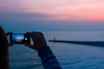 girl takes a picture on mobile phone sunset in the evening at sea