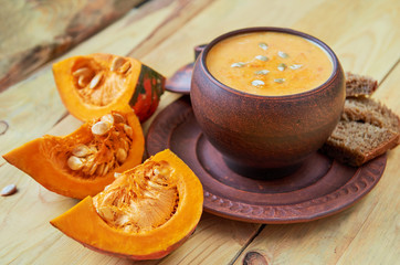 Bowl of hot pumpkin soup with sliced yellow pumpkins and seeds on the wooden background. Traditional autumn food or thanksgiving dish. Side view