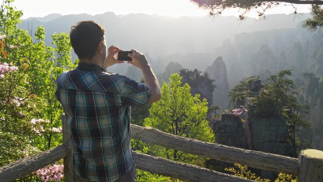 Man tourist taking pictures of mountain landscape at sunset with his smartphone. UHD, 4K