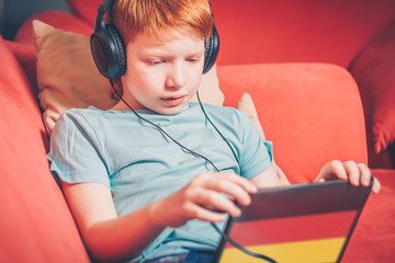 Red-haired boy sitting on the sofa learn German on the tablet