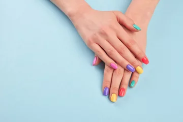 Rolgordijnen Hands with beautiful manicured nails. Girl hands with beautiful summer manicure on blue background in studio. Manicured hands and copy space. © DenisProduction.com