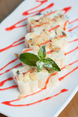 Close-up - mint leaves on creamy dessert in white chocolate sprinkled with ground nuts and berry sauce served on a white plate. Restaurant menu
