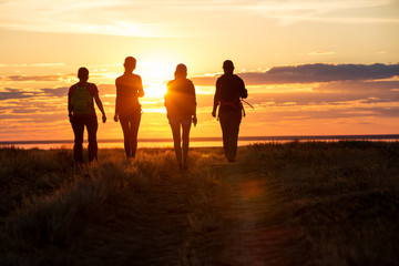 A group of people walking in a track. They go against the background of the orange sun, their...