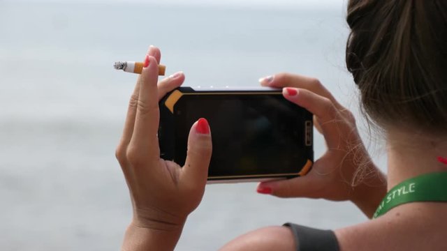 Female holding smoking cigarette and smartphone mobile as she shoot video for social media