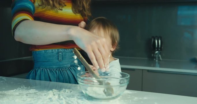 Young mother teaching her toddler son how to bake